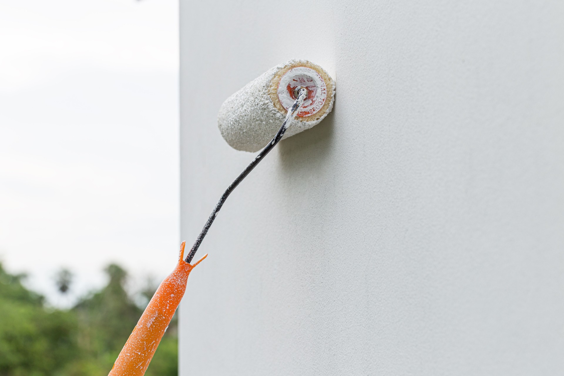 Painting an exterior wall with a white paint roller brush, outdoor home renovation concept.